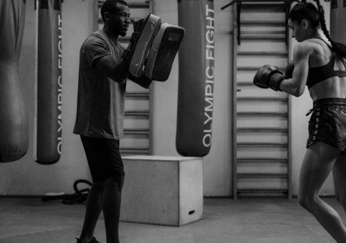 A boxer practicing with a trainer using focus mitts in a gym setting.
