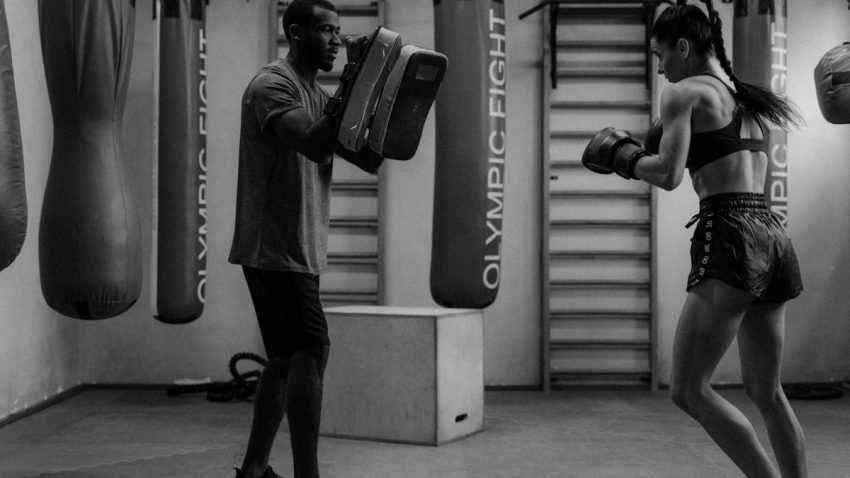 A boxer practicing with a trainer using focus mitts in a gym setting.